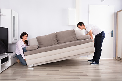 Two people lifting a sofa off the floor